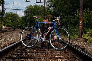 Man working on a bike with Union Jack flag painted on the frame and Selle Anatomica leather saddle sitting on train tracks