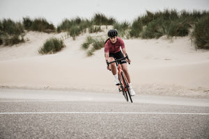 Woman pedaling around a curve in the road while cycling by a sandy beach