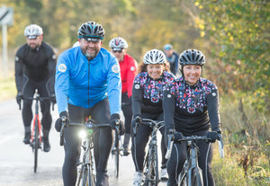 A group of cyclists riding along a country lane smiling