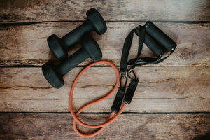 Orange and black resistance bands and small black dumbbells on a wood surface