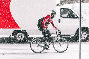 Man pedaling bike in snow next to a delivery truck