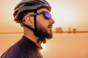 Head shot of a man in cycling helmet and sunglasses looking away with a sunset over water in the background