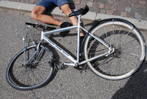 Legs of man lying on the ground under a wrecked bicycle after an accident