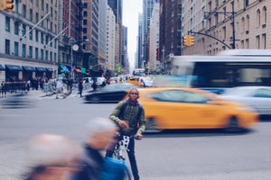 Man riding his bike through a busy urban intersection while cars speed by behind him