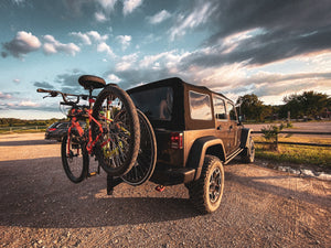 Jeep parked in a gravel lot with two bicycles on a rear bike rack 