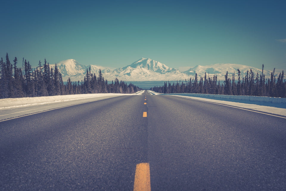 Alaskan road in winter with snow along the sides and snow-covered mountains ahead