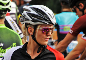 Blonde woman in a cycling helmet and sunglasses looking to the side in a crowd of cyclists
