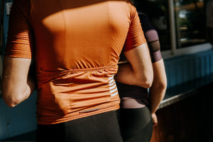 Backside of a man wearing an orange cycling jersey with three pockets across the back