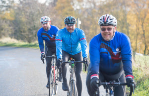 Group of three male cyclists in blue jackets and jerseys riding their bikes along a country lane in the Yorkshire countryside