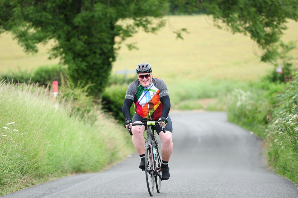 Large man in a multicolor cycling jersey riding his bike on a country road and smiling