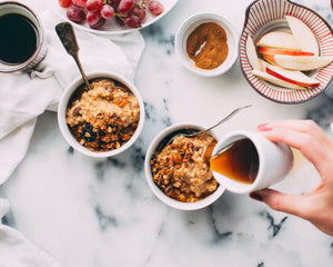 Overhead view of person’s hand pouring syrup over bowls of granola and oatmeal