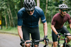 Two men cycling side by side up a hill and exerting a lot of energy as they pedal