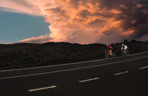Two cyclists coasting down a hill at sunset