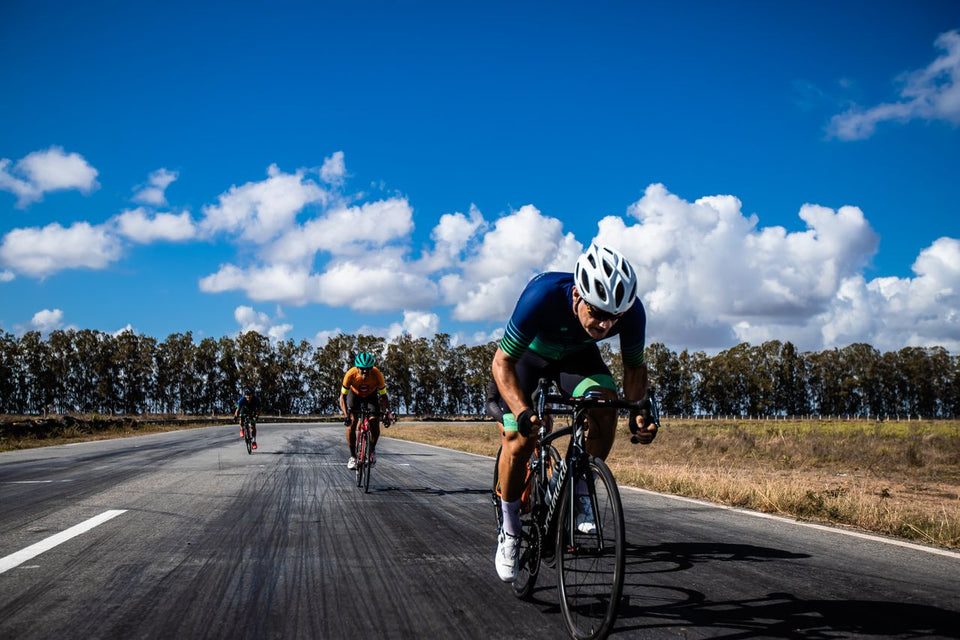 Competitive cyclists speeding on an open road in João Pessoa, Brazil, under a clear blue sky.