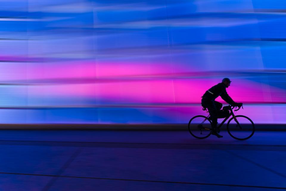 Silhouette of a man cycling in the dark with colored lights on the background wall