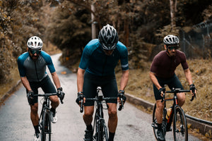 Front view of three men cycling uphill and standing on their bikes as they pedal