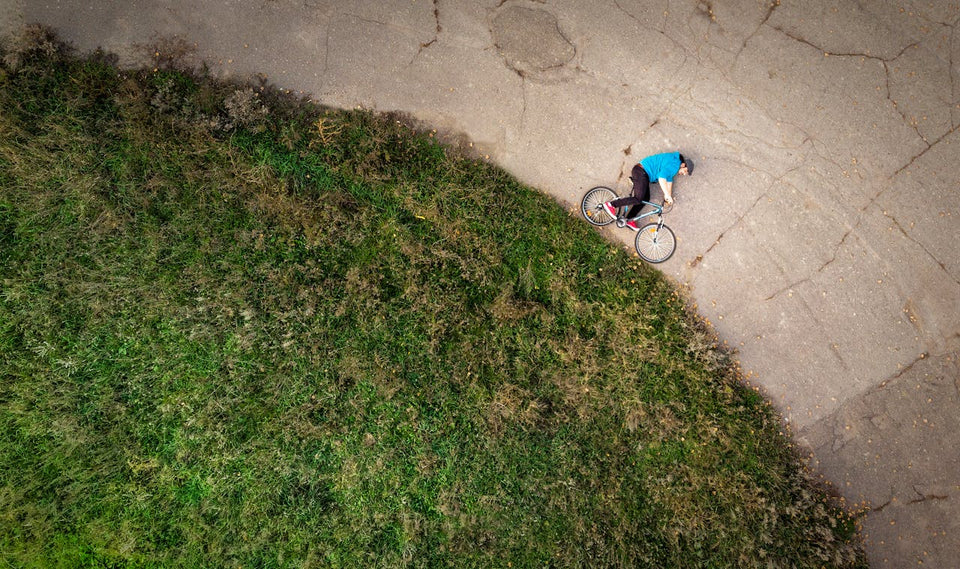 Overhead view of man fallen with bicycle on pavement next to grass