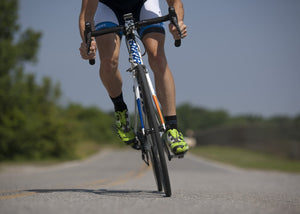 Front view of lower body of a cyclist standing, pedaling and tilting into a turn