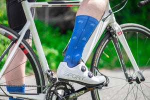 Legs of a cyclist on a bike, wearing blue socks and white cycling shoes