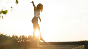 Woman balancing on a fence with the sun setting in the background
