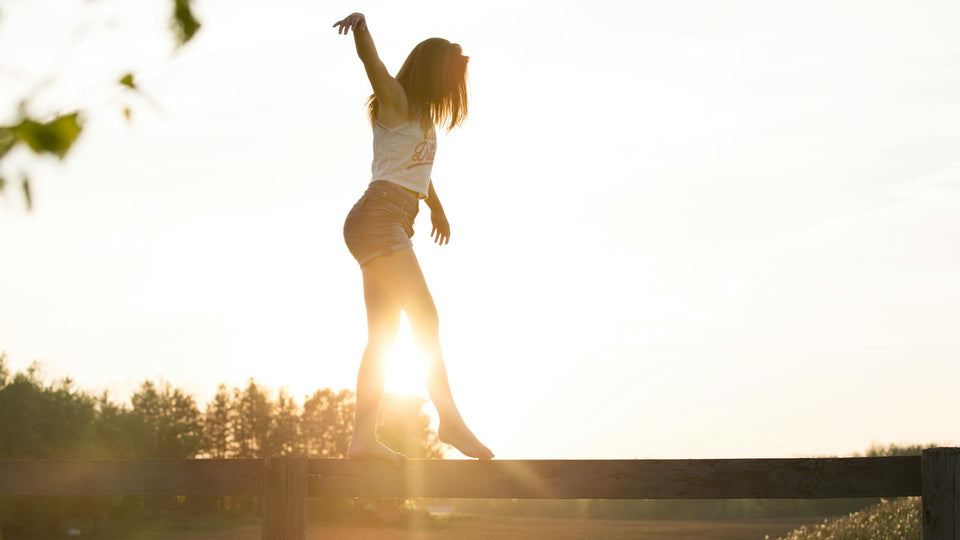 Woman balancing on a fence with the sun setting in the background