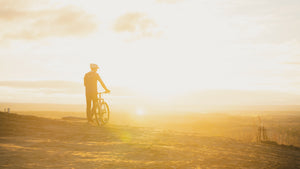 Cyclist standing by his bike on a trail at sunset