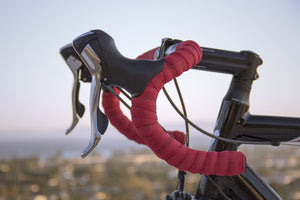 Close-up of red road bike handlebars with black hoods and silver brake handles