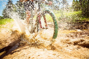 Close-up of cyclist’s wheel splashing through mud on a dirt trail