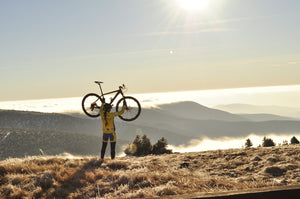 Woman holding bicycle above head and looking down over hilltops