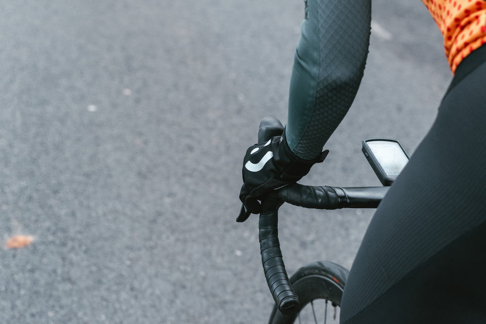Side of a cyclist's hand with smiley-face glove, gripping the hoods of their handlebars as they pedal