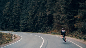 Rear view of a man cycling around a bend in a two-lane road next to a forest