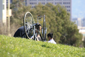 Man and his child fixing a bike on a grassy hill near a city street