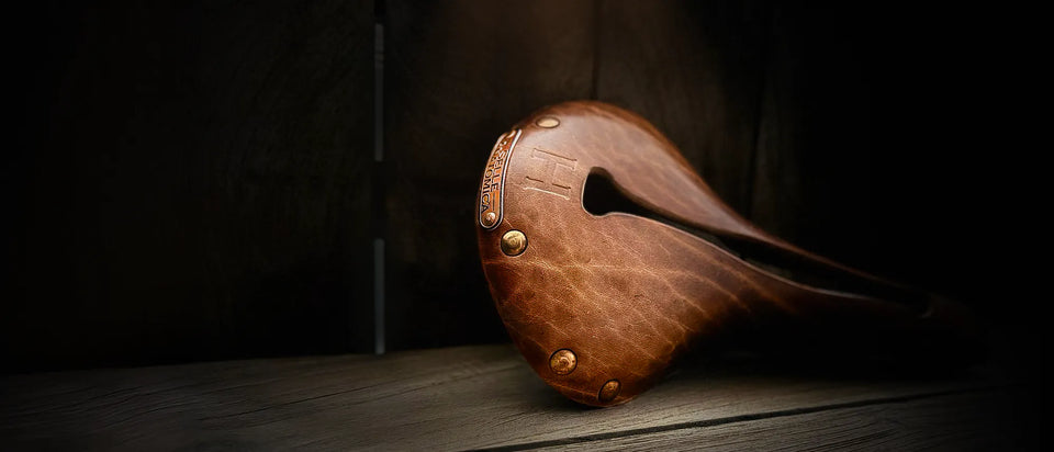 Brown leather bike saddle (Selle Anatomica H1 model) propped up against a wooden backdrop