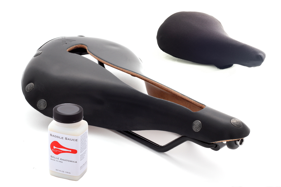 A black waterproof bike seat cover and a bottle of Saddle Sauce, displayed beside a Selle Anatomica bicycle saddle for demonstration